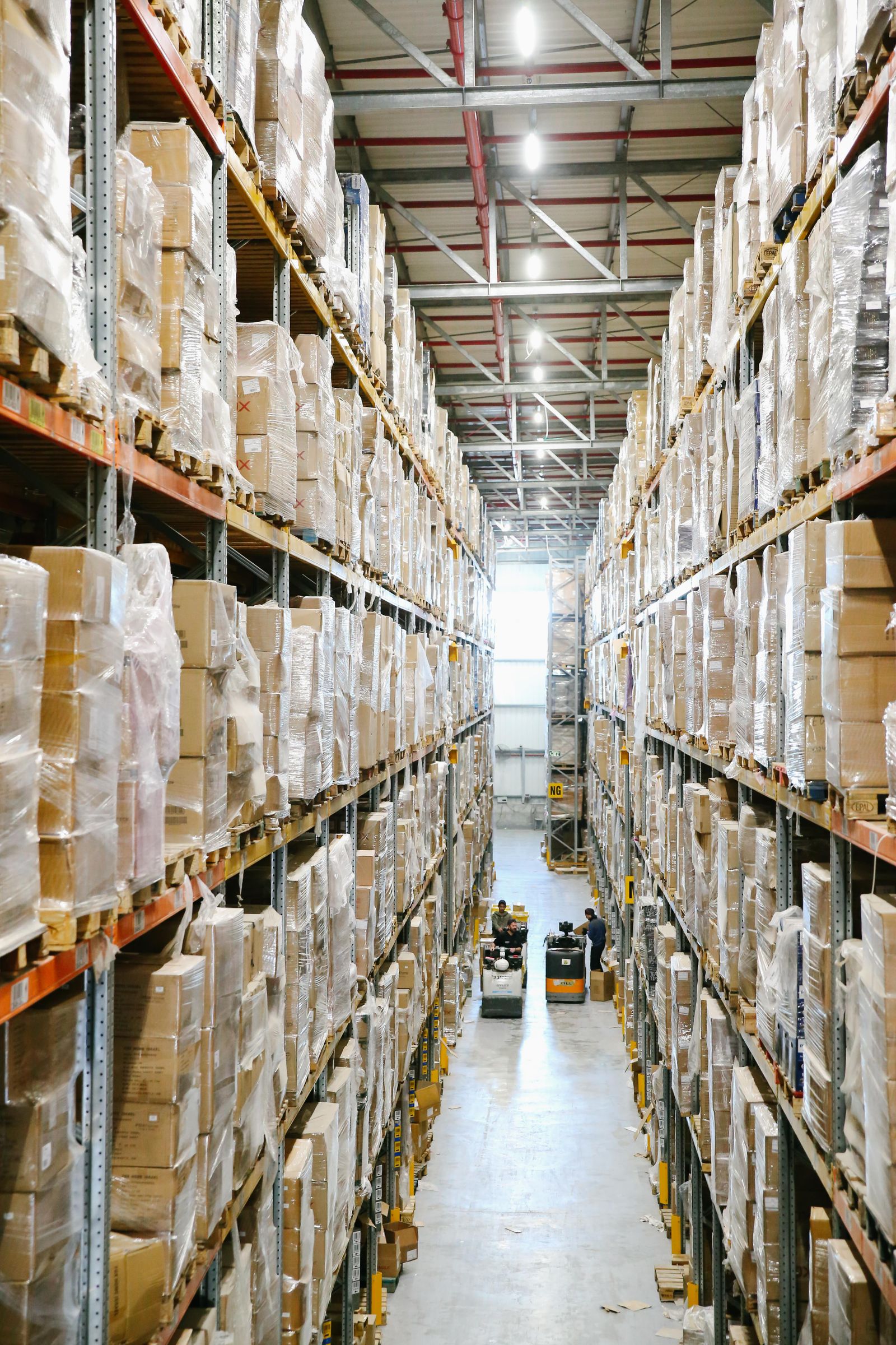 Stocked warehouse aisle with staff moving goods on a pallet truck